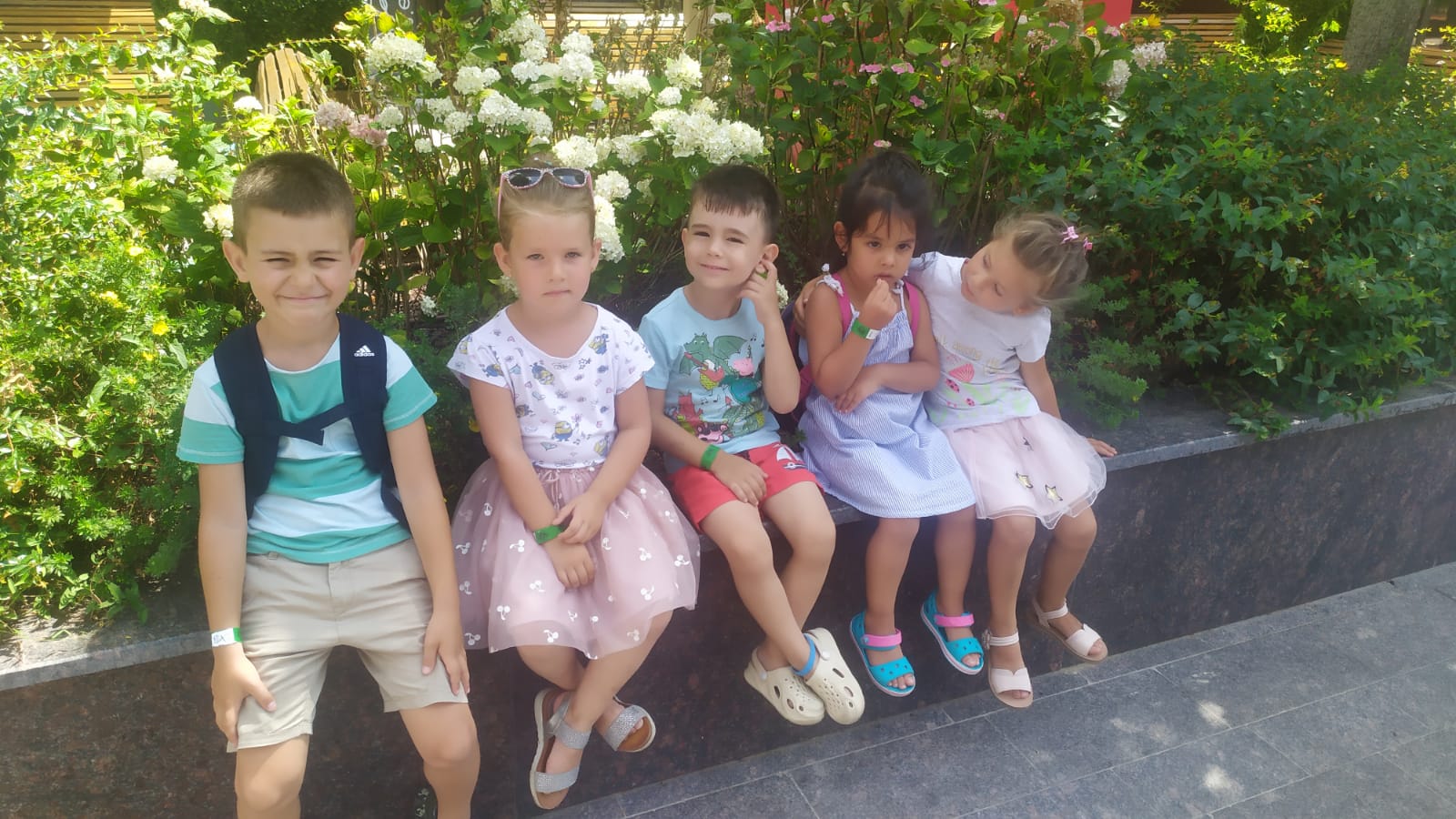 Five kids sitting nex to each other on a stone bench