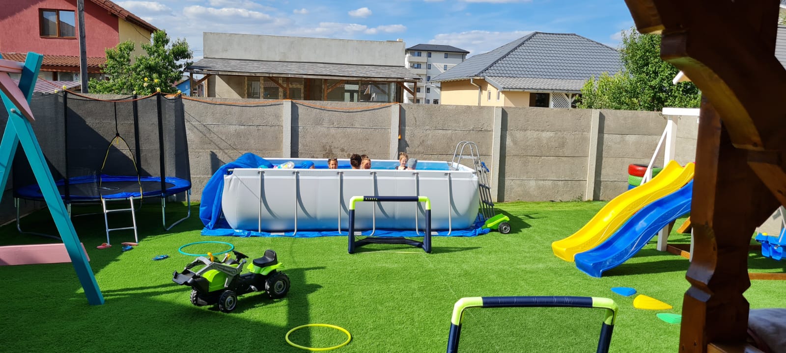 A green area in a garden with a pool and toys around it