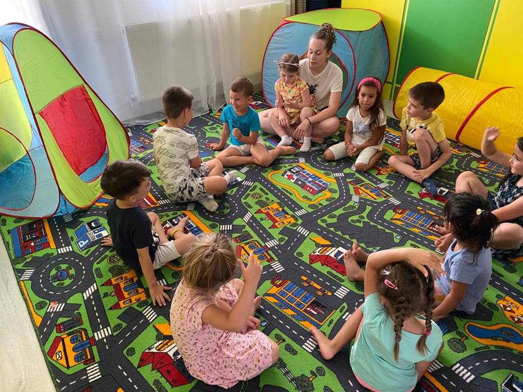 A group of kids chatting, sitting down in a circle on a colorful carpet