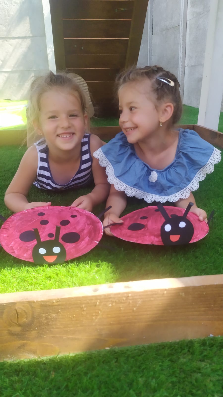 Two gils laying on their bellies showing their ladybugs made out of carbord