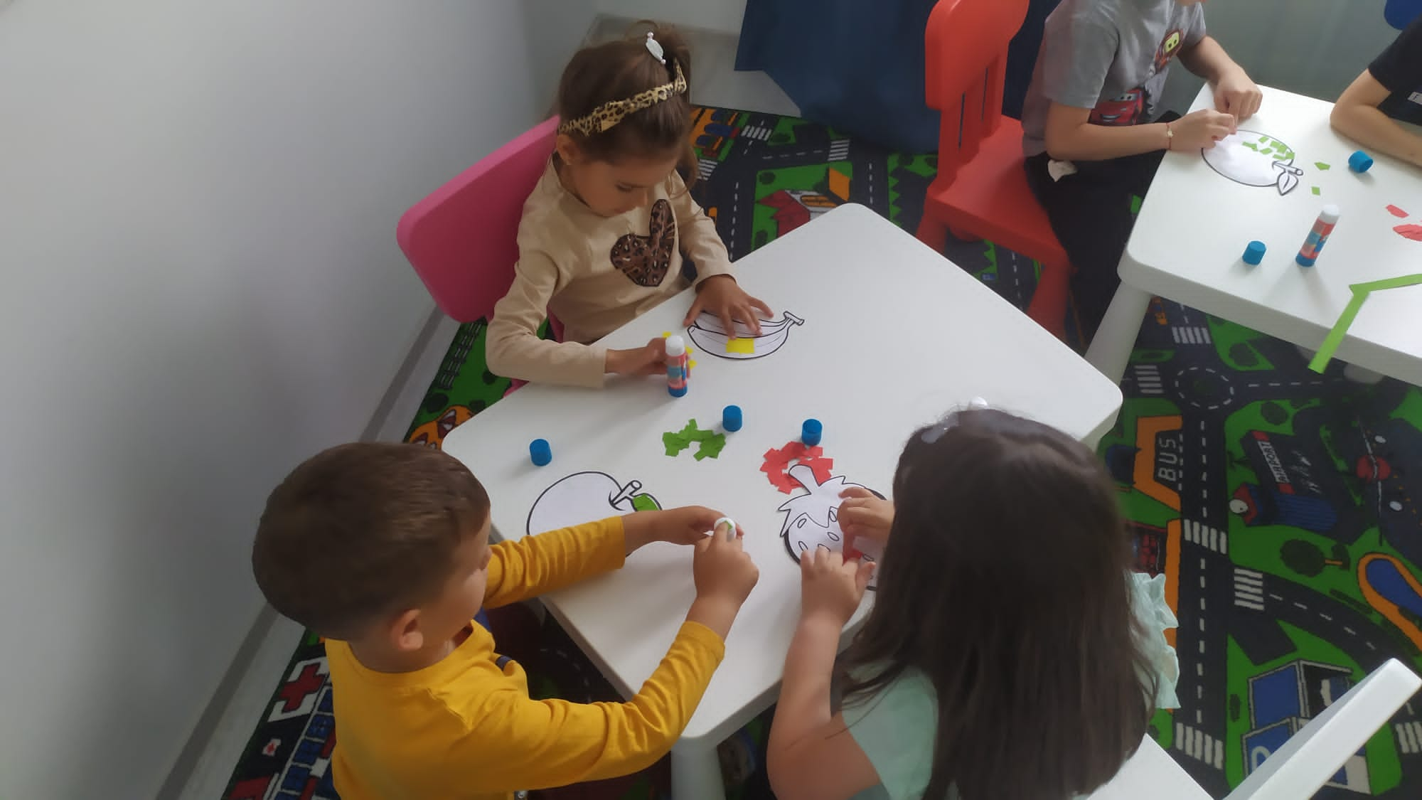 Three kids sitting around a small table, coloring